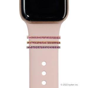 May include: Three pink, gold, and silver watch band charms with pink rhinestones. The charms are shown on a pink silicone watch band.