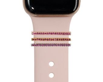 May include: Three pink, gold, and silver watch band charms with pink rhinestones. The charms are shown on a pink silicone watch band.