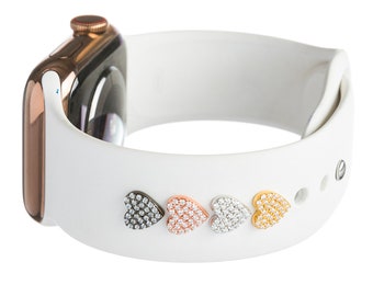 May include: White Apple Watch band with five heart-shaped charms. The charms are black, rose gold, silver, and gold, and each is encrusted with clear rhinestones.