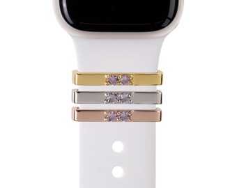 May include: Three Apple Watch band attachments with two small purple gemstones on each. The attachments are gold, silver, and rose gold.