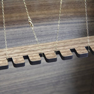 May include: Close-up of a wooden jewelry box with multiple slots for hanging necklaces. The slots are lined with black felt and the box has a natural wood finish.