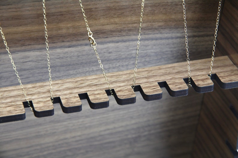 May include: Close-up of a wooden jewelry box with multiple slots for hanging necklaces. The slots are lined with black felt and the box has a natural wood finish.