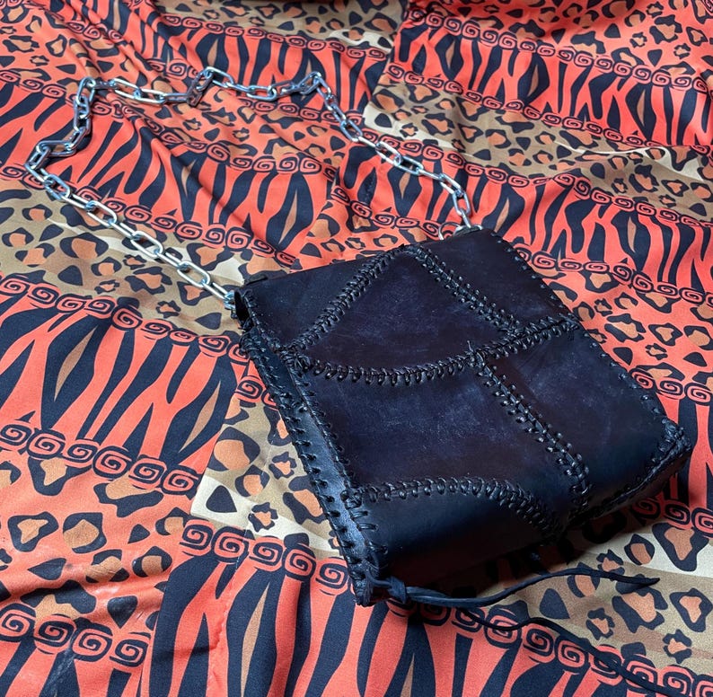 Pu&ograve; includere: Una borsa a tracolla in pelle nera con patchwork e una catena argentata. La borsa ha un design unico con pi&ugrave; pannelli cuciti.