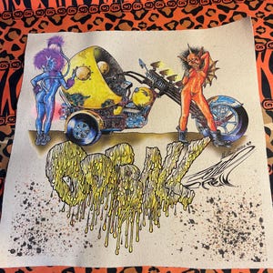 May include: A colourful illustration of a motorcycle with a yellow, round, bubble-like sidecar. Two figures, one blue and one red, are riding the motorcycle. The word "GRAVE" is written in yellow dripping paint.