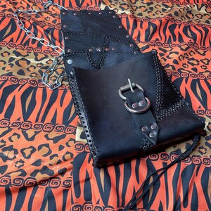 Pu&ograve; includere: Una borsa in pelle nera con una fibbia argentata e una tracolla a catena. La borsa ha un design a patchwork sul davanti ed &egrave; decorata con borchie argentate.