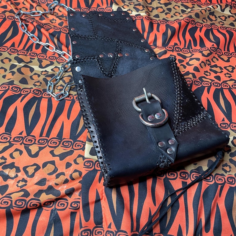 Pu&ograve; includere: Una borsa in pelle nera con una fibbia argentata e una tracolla a catena. La borsa ha un design a patchwork sul davanti ed &egrave; decorata con borchie argentate.