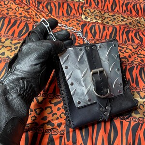 Pu&ograve; includere: Una borsa in pelle nera con un pannello in metallo argentato e una fibbia nera. La borsa ha una tracolla a catena ed &egrave; decorata con borchie argentate.