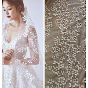 May include: White bridal veil with delicate floral embroidery. The veil is made of soft tulle and features a delicate pattern of leaves and flowers. The veil is perfect for a wedding or other special occasion.