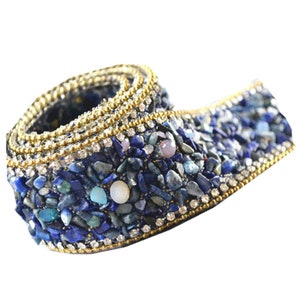 Pode incluir: Uma fita azul e dourada com borda de contas e um design de pequenas pedras azuis e strass.