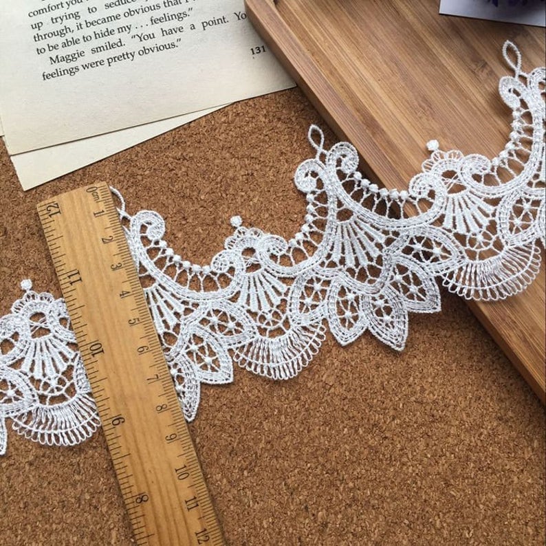May include: White lace trim with a scalloped edge. The trim is approximately 3 inches wide and is measured with a ruler.