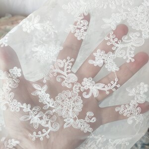 May include: White sheer fabric with a delicate floral embroidery pattern.
