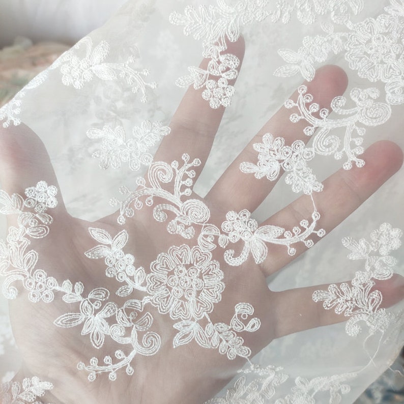 May include: White sheer fabric with a delicate floral embroidery pattern.