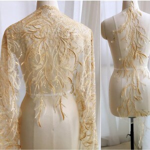 Könnte beinhalten: Goldene Spitzenstoff mit einem zarten Blumenmuster. Die Spitze ist durchsichtig und hat eine weiche, fließende Textur.