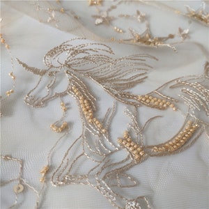 May include: Gold embroidered unicorn design on a sheer white fabric. The unicorn is outlined with gold thread and has gold beads sewn along its mane and body.