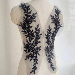 Puede incluir: Aplique de encaje floral negro con un delicado diseño de hojas. El aplique está hecho de tejido de malla y es perfecto para agregar un toque de elegancia a cualquier prenda.