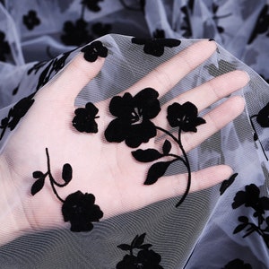 May include: Black floral embroidery on sheer white fabric. The fabric is delicate and has a soft, flowing texture.