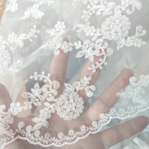 May include: White sheer fabric with delicate floral embroidery. The fabric has a soft, flowing texture and is perfect for creating elegant garments or accessories.