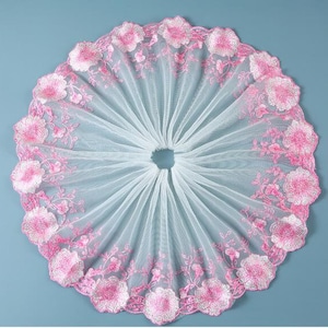 May include: White tulle fabric with pink floral embroidery. The fabric is gathered in a circle and has a scalloped edge.