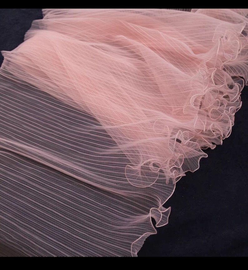Peut inclure: Gros plan sur un tissu rose p&acirc;le d&eacute;licat, &agrave; texture pliss&eacute;e. Le tissu est transparent et pr&eacute;sente un bord festonn&eacute;. Le mat&eacute;riau semble l&eacute;ger et fluide, adapt&eacute; &agrave; l'habillement ou &agrave; des fins d&eacute;coratives.