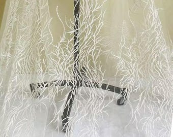 May include: White sheer fabric with an embroidered botanical design. The delicate pattern features thin, branching lines resembling leaves or twigs. The fabric is draped over a black stand, showcasing its texture and transparency.