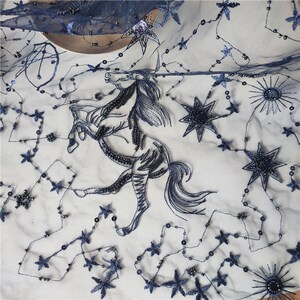 May include: Black embroidered lace fabric with a horse design and stars. The fabric is sheer and has a delicate texture.