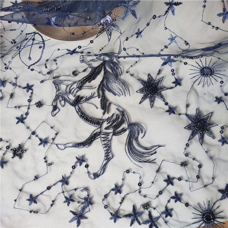 May include: Black embroidered lace fabric with a horse design and stars. The fabric is sheer and has a delicate texture.