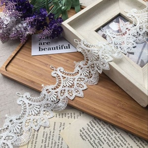 May include: White lace trim with a delicate floral pattern. The lace is shown on a wooden surface with a card that says "you are beautiful".