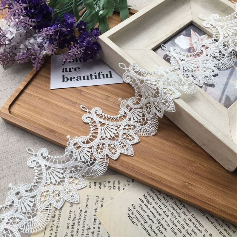 May include: White lace trim with a delicate floral pattern. The lace is shown on a wooden surface with a card that says "you are beautiful".