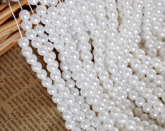 May include: A strand of white pearl beads. The beads are round and smooth, and they are strung on a white thread.