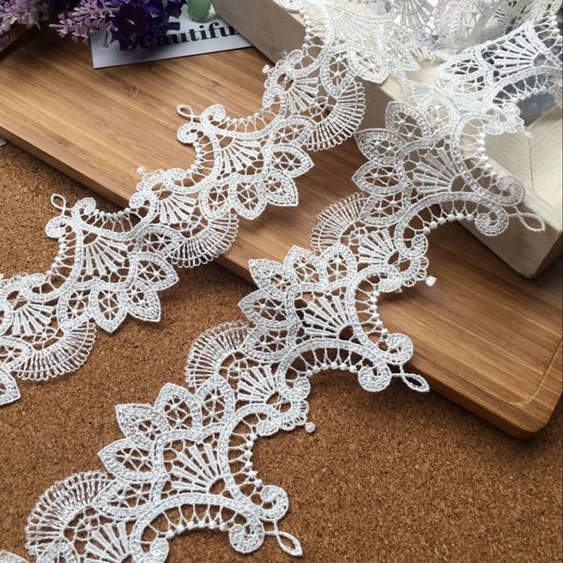 May include: White lace trim with a delicate floral pattern. The lace is about 2 inches wide and has a scalloped edge.