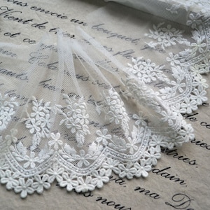 May include: White lace trim featuring a delicate floral design. The lace is made from a soft, sheer fabric and has a scalloped edge.