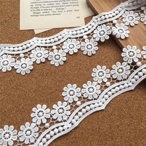 May include: White lace trim with a scalloped edge and small flower designs. The trim has a repeating pattern of small flowers and beads.