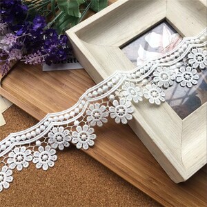 May include: White lace trim with a scalloped edge and small flower designs. The lace is delicate and intricate, and it would be perfect for adding a touch of elegance to any project.