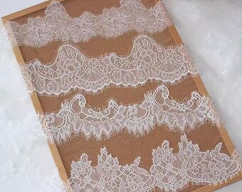 May include: Four strips of white lace with intricate floral and scrollwork patterns. The lace is displayed on a wooden frame with a brown background, showcasing the delicate details and textures of the fabric.