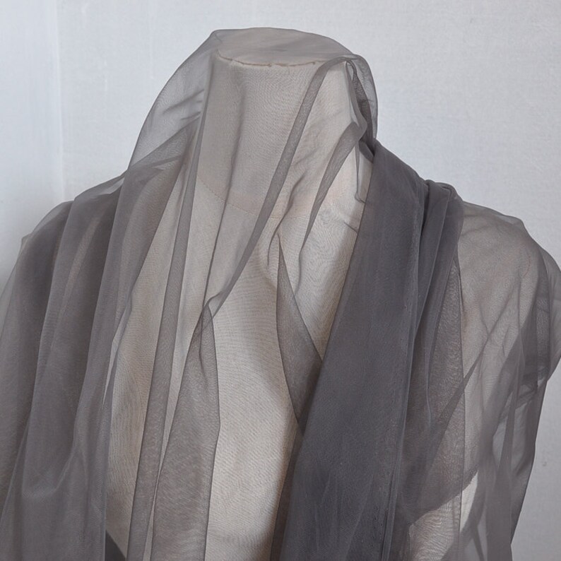 Pu&ograve; includere: Un tessuto grigio trasparente drappeggiato su un manichino. Il tessuto &egrave; leggero e traslucido, con una texture morbida e fluida.