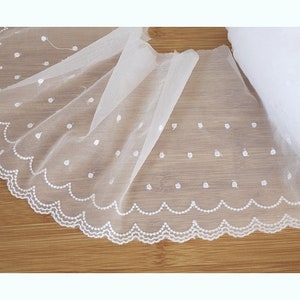 Pode incluir: Renda branca com borda festoneada e pequenos pontos brancos. A renda é delicada e transparente.