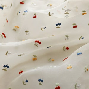 K&ouml;nnte beinhalten: Wei&szlig;er, durchsichtiger Stoff mit einem zarten Stickmuster aus bunten Kirschen. Die Kirschen sind rot, blau, gelb und gr&uuml;n.