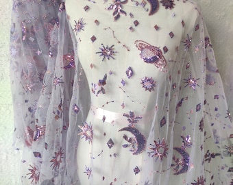 May include: Purple sheer fabric with a delicate pattern of stars, moons, and other celestial shapes. The fabric is embellished with sequins and beads, creating a shimmering effect.