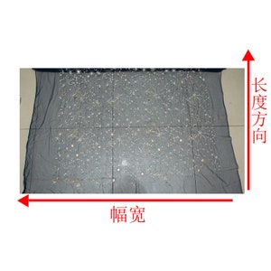 May include: A sheer, dark gray fabric with an embroidered celestial design. The embroidery features gold and silver stars, moons, and other shapes. The fabric is rectangular and appears to be a decorative textile.