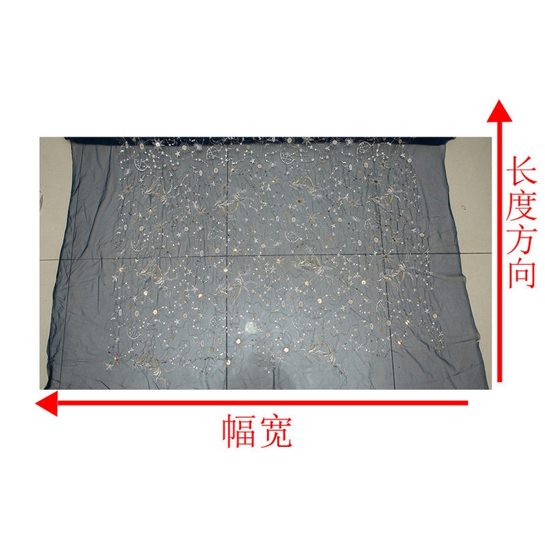 May include: A sheer, dark gray fabric with an embroidered celestial design. The embroidery features gold and silver stars, moons, and other shapes. The fabric is rectangular and appears to be a decorative textile.