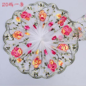 May include: White mesh fabric with embroidered pink, yellow, and orange flowers and green leaves. The fabric has a scalloped edge and is decorated with small gold sequins.