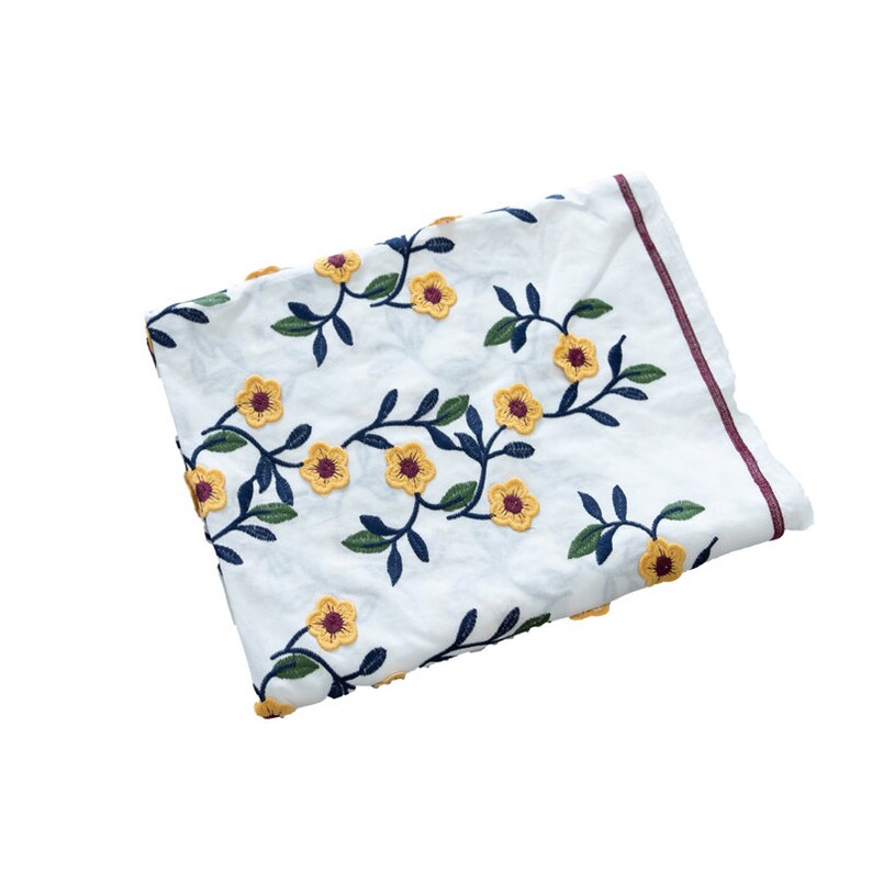 May include: White fabric with embroidered yellow flowers and dark blue stems. The fabric is folded and has a burgundy border.
