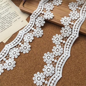May include: White lace trim with a scalloped edge and small white beads. The lace has a delicate floral pattern.