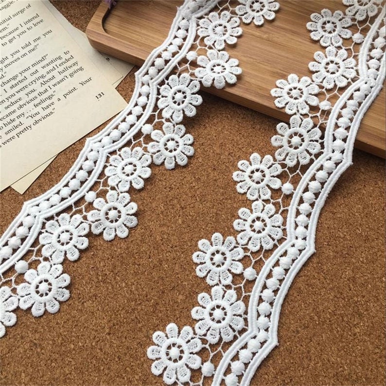 May include: White lace trim with a scalloped edge and small white beads. The lace has a delicate floral pattern.