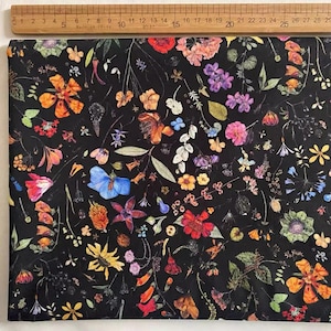 May include: Black fabric with a repeating pattern of colourful pressed flowers and leaves. The fabric has a dark black background with a variety of flowers in shades of red, pink, blue, yellow, and green.