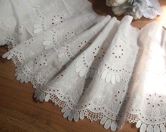 May include: White cotton lace trim with a scalloped edge and delicate eyelet details. The lace has a repeating pattern of circles and swirls.