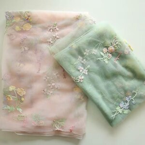 May include: Two layers of sheer fabric with floral embroidery. The top layer is pink with white and light pink flowers. The bottom layer is green with white and light green flowers.