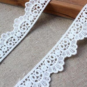 May include: White lace trim featuring a delicate floral design. The trim has a scalloped edge and is ideal for adding a touch of elegance to any project.