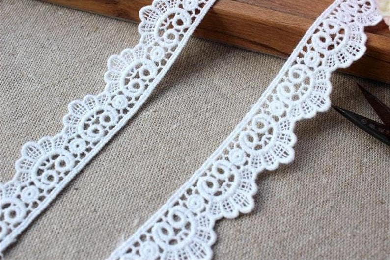 May include: White lace trim featuring a delicate floral design. The trim has a scalloped edge and is ideal for adding a touch of elegance to any project.