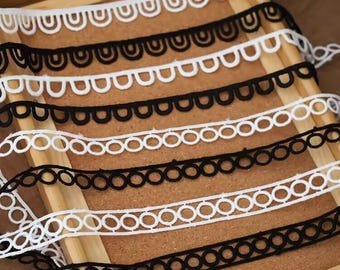 Puede incluir: Una colección de cintas decorativas con patrones geométricos repetitivos en blanco y negro. El surtido incluye bordes festoneados con motivos de arco y bandas rectas con recortes circulares, dispuestos en filas paralelas.